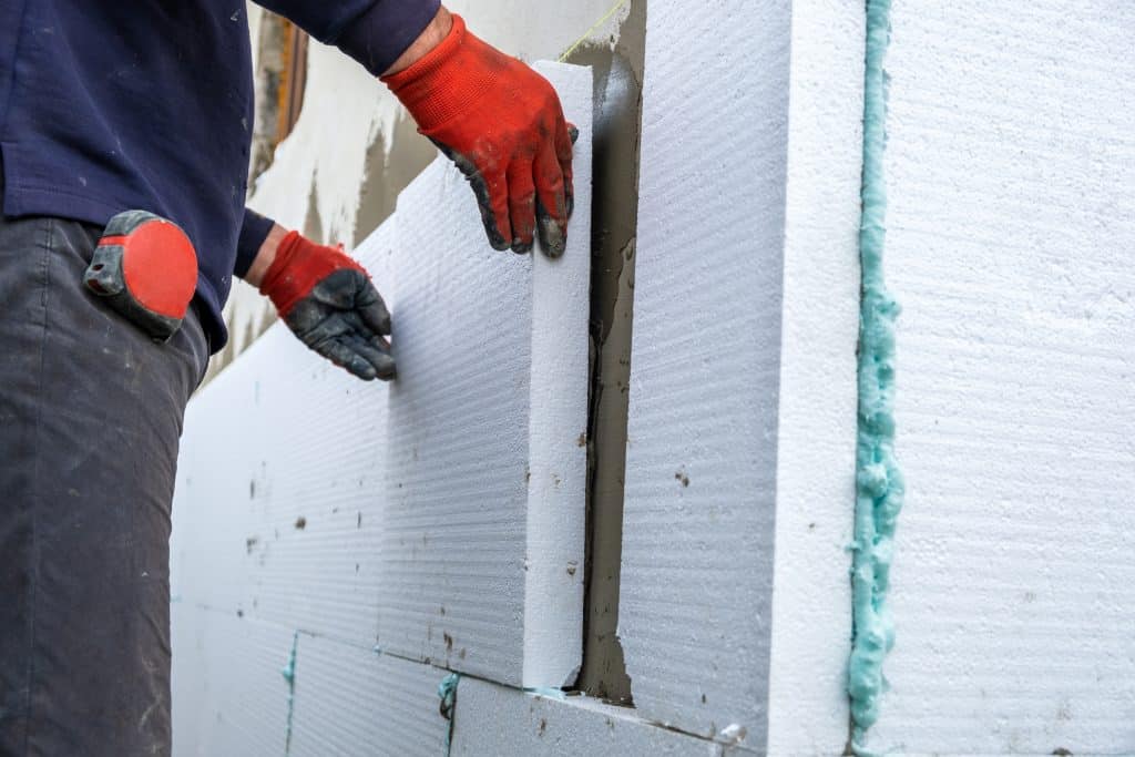 Ouvrier de construction installant des plaques d'isolation en polystyrène sur le mur de la façade d'une maison