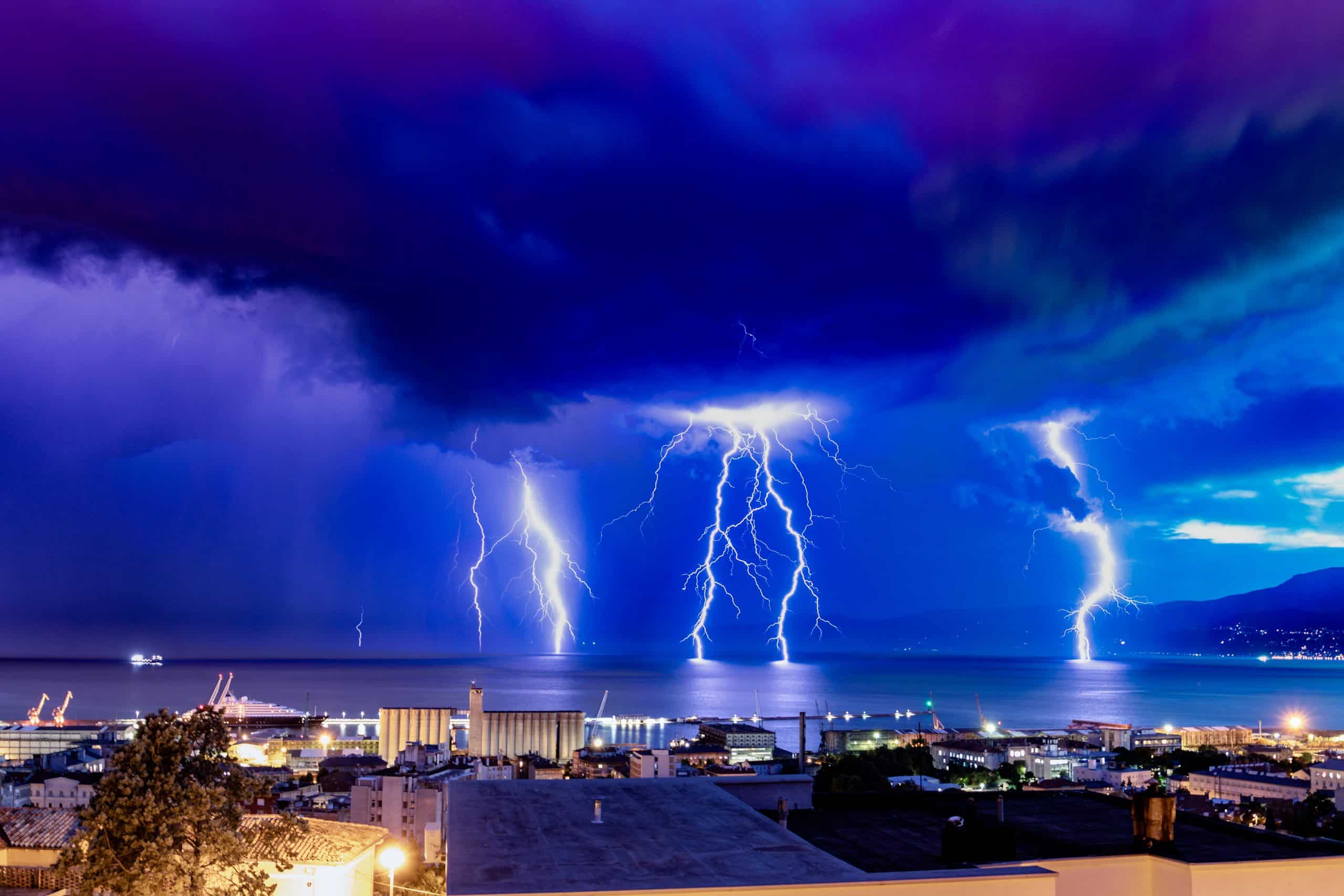 lightnings striking on the ocean from gloomy skies at night framed with coastal buildings