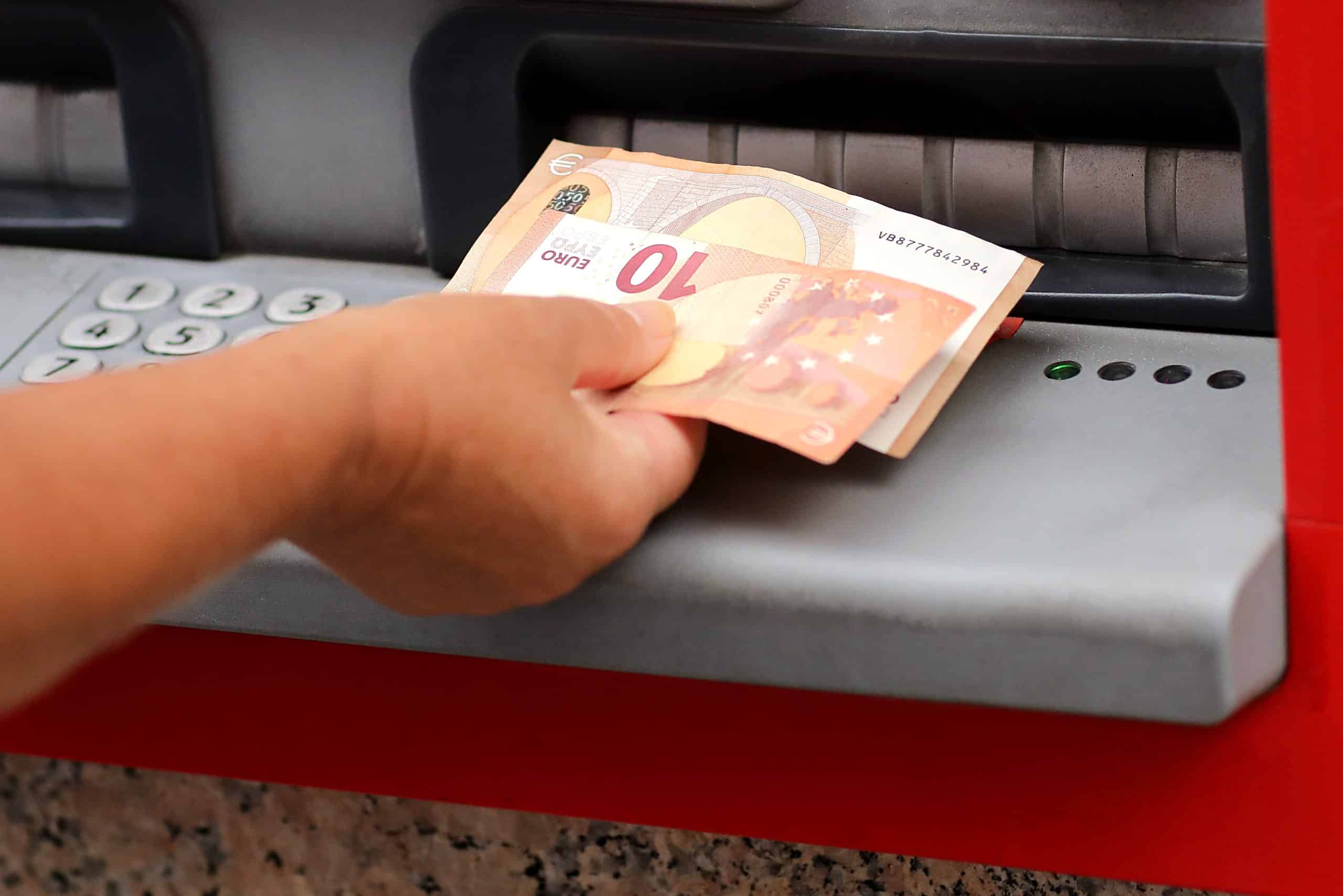 withdrawing euros from an atm from bank outdoors in europe city. adult female hand holding european banknotes denominations 10 and 50 euros from automatic cash machine. salary, pension, deposit