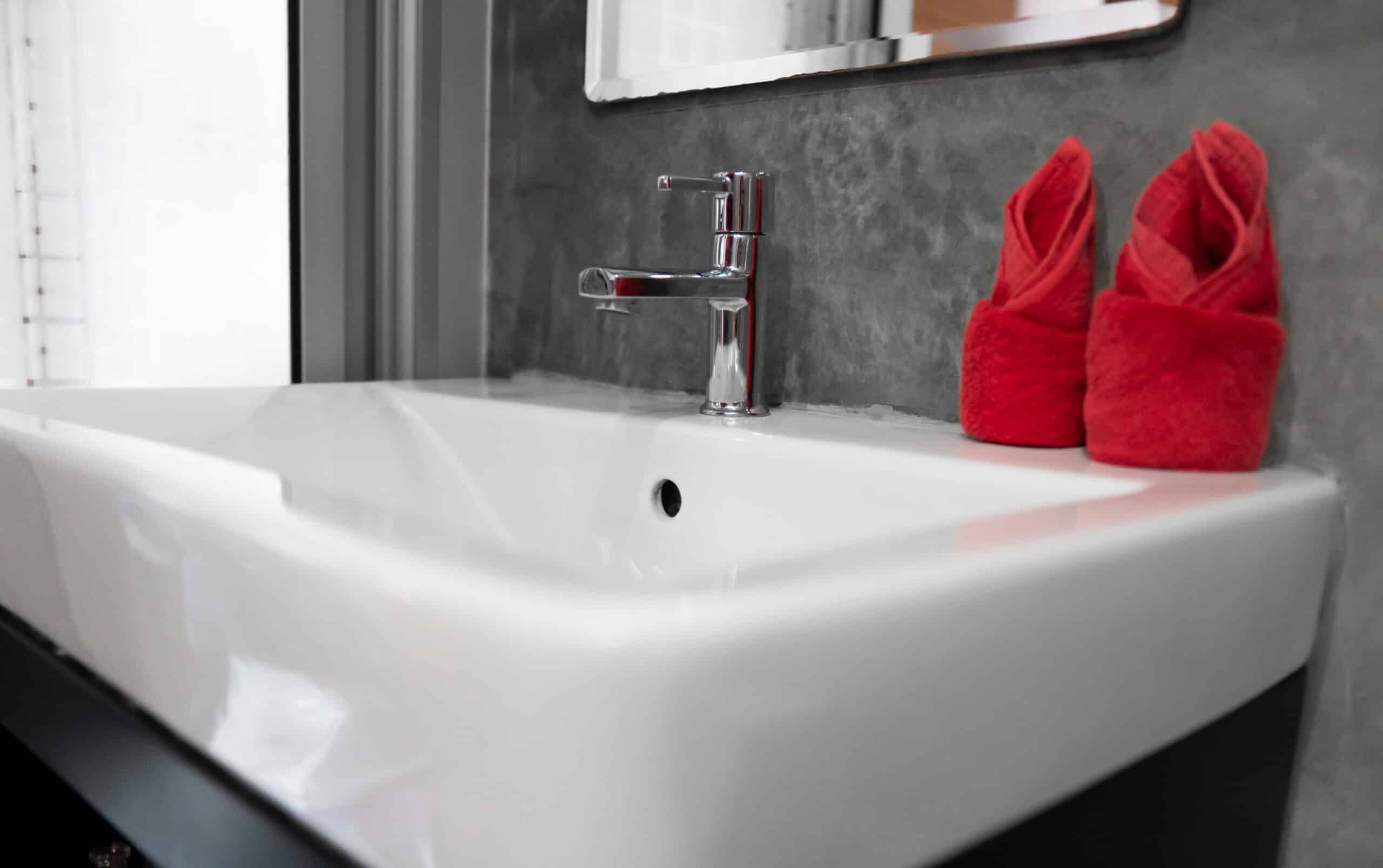 modern stainless steel faucet with wash basin sink with a two red towels on it . counter bathroom interior contemporary. luxury and stylish design bathroom with a concrete style walls.